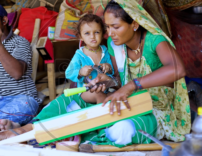 A local women cricket bat maker making bats with having her son on her lap.