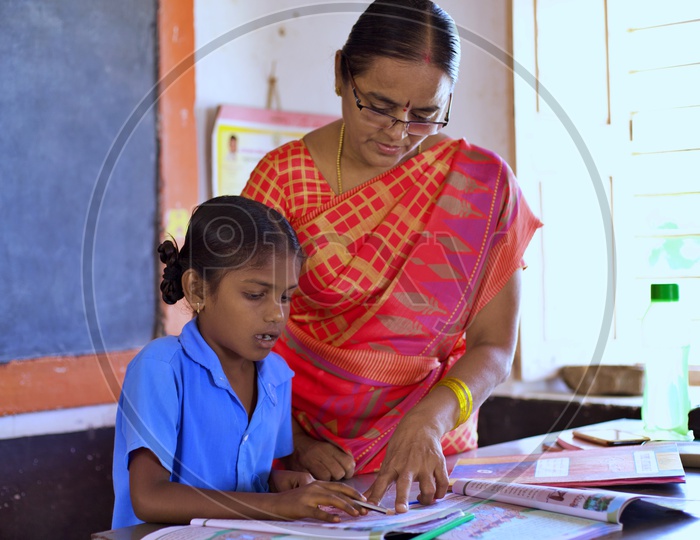 A govt teacher teaching a girl student how o read.