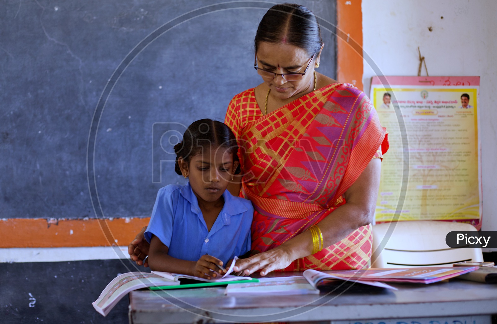 A Govt teacher teaching a girl student how to read.