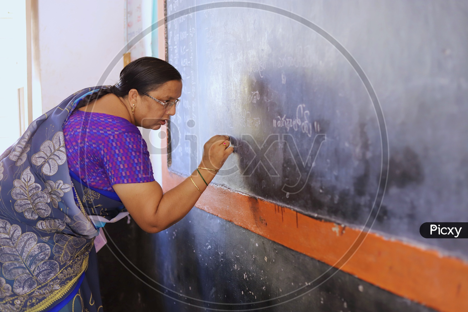 A Govt teacher writing on a blackboard.