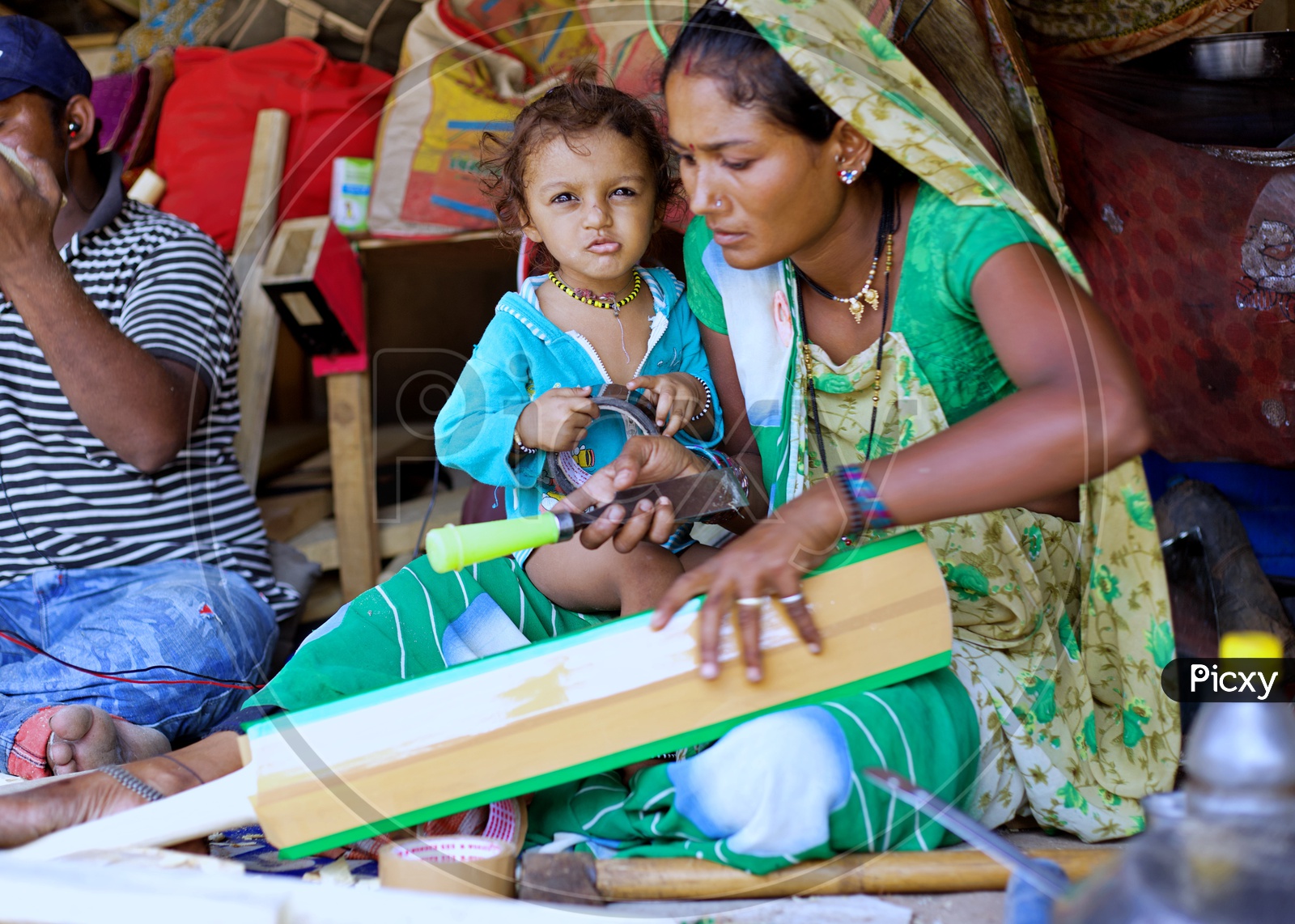 A local women cricket bat maker making bats with having her son on her lap.