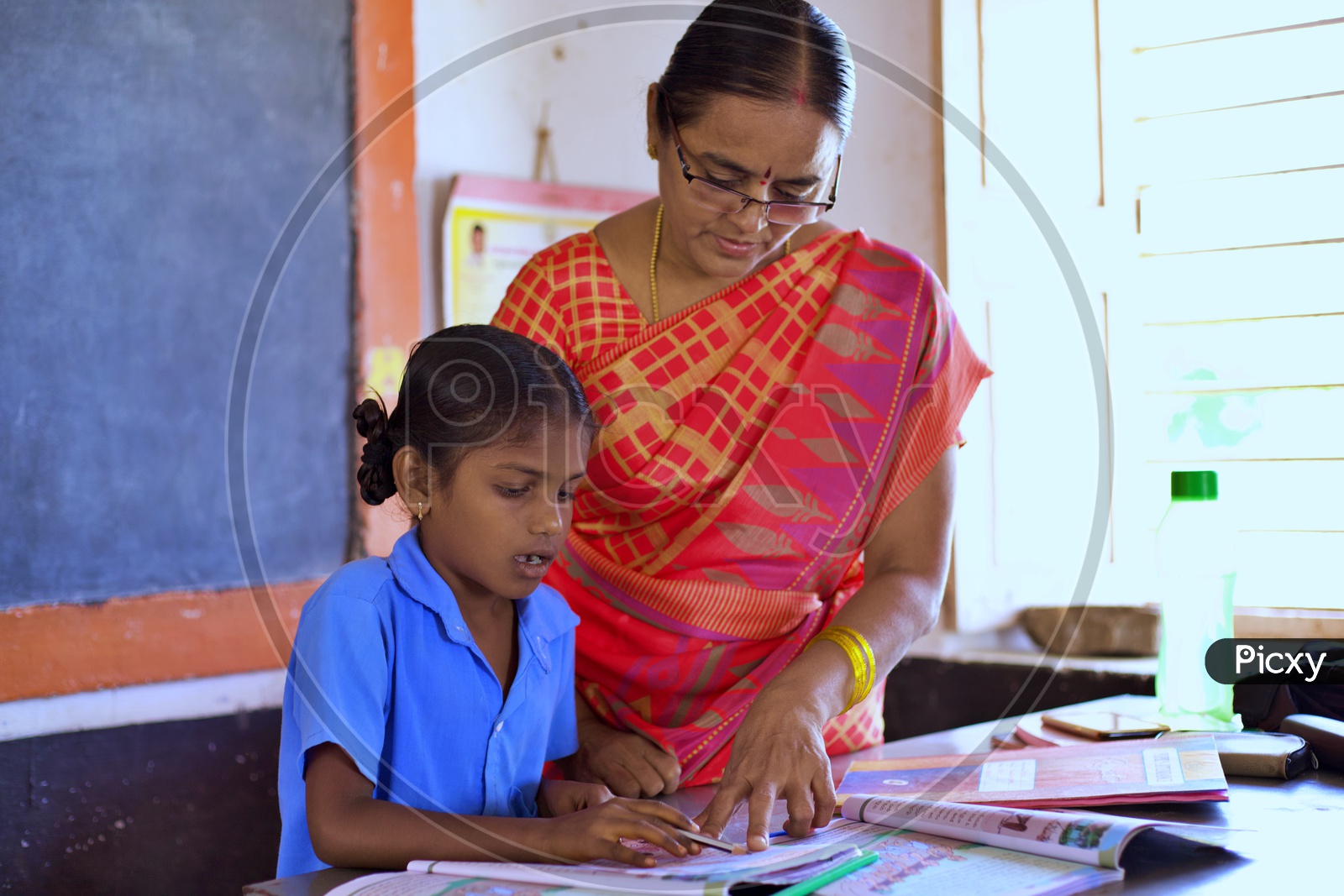 A govt teacher teaching a girl student how o read.