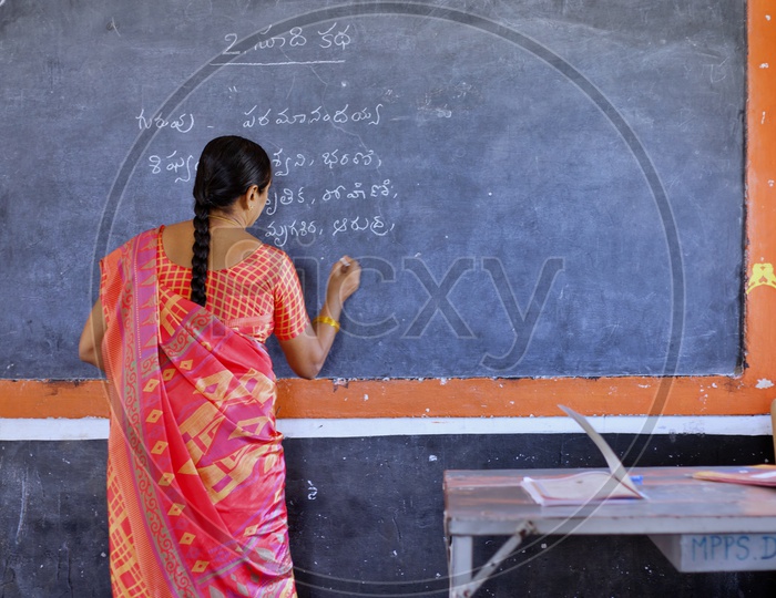 A Govt school teacher writing on a blackboard.