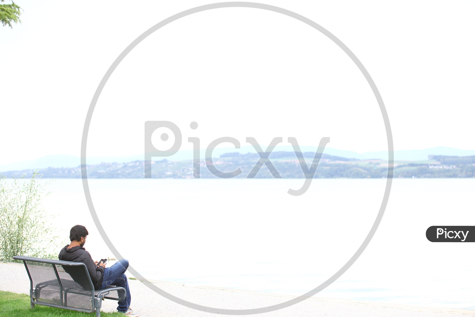 A Man Using Mobile By Sitting  alone On the Bank of a Lake