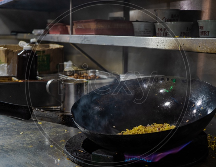 Noodles being cooked in a wok with smoke
