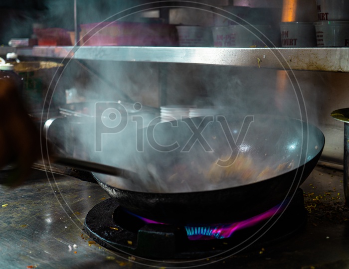 Person cooking noodles in a wok with smoke