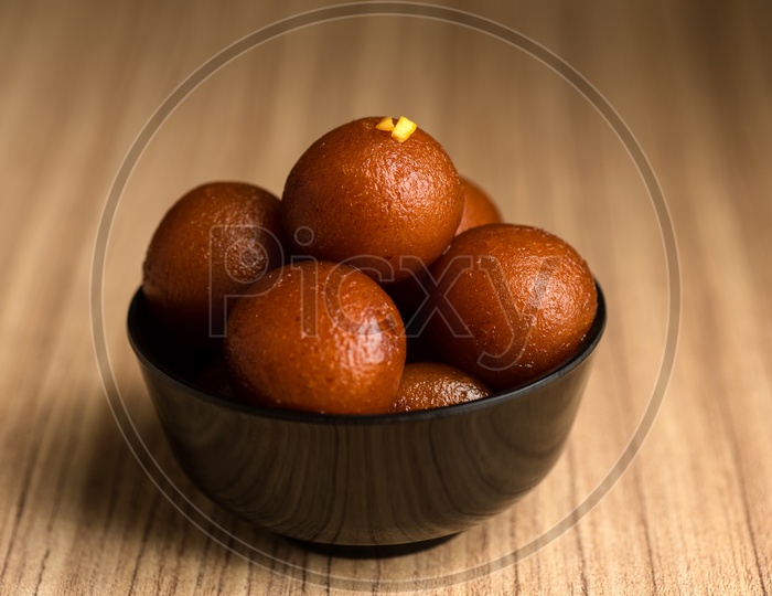 Gulab jamun  Indian Sweet Served In a Black Ceramic Bowl on an Wooden Background