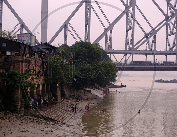 People Taking Dip in Hooghly River with Howrah Bridge in Background