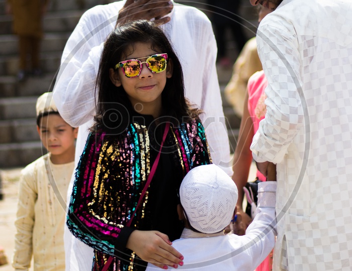 A girl wearing sunglasses with her family in traditional clothes during Eid celebrations in at a mosque in Delhi