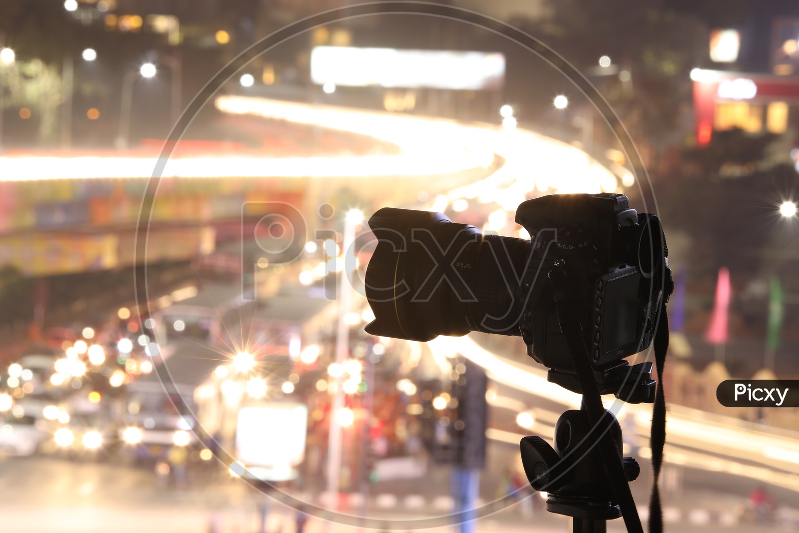 Silhouette of a DSLR Camera Mounted To a Tripod With Aerial View Of Traffic Vehicle Lights Bokeh Background