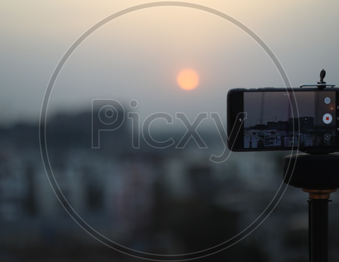 Mobile Phone Smartphone Tagged To a Tripod And Shooting Sunset Over a City Scape With High Rise Construction Buildings