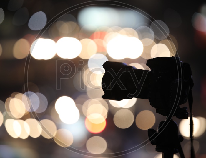 Silhouette of a DSLR Camera Mounted To a Tripod With Aerial View Of Traffic Vehicle Lights Bokeh Background