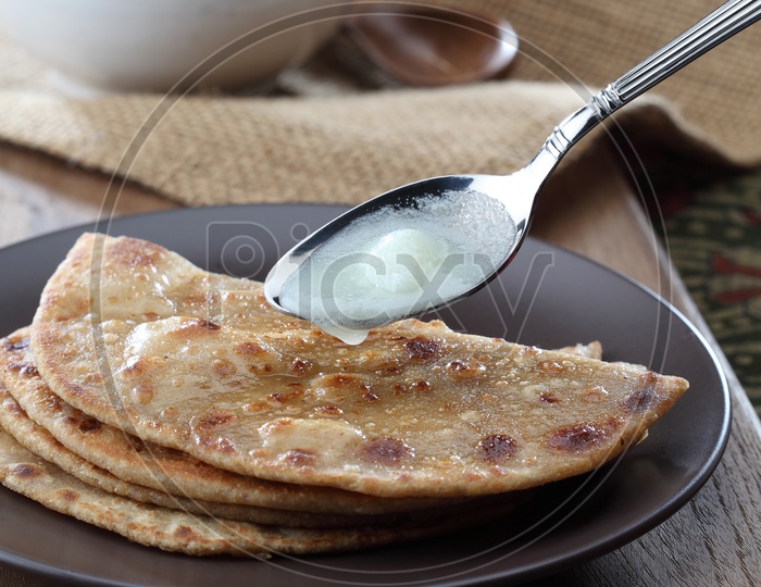 Desi Ghee in a spoon being applied on a parantha.