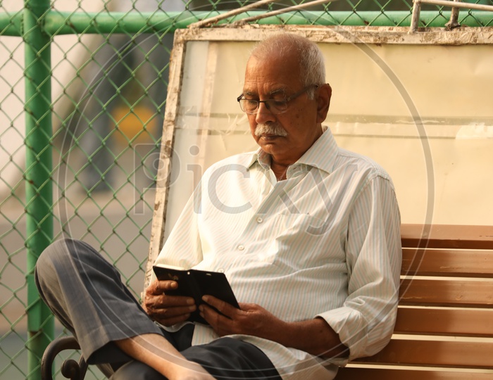 An Old Man Checking Smartphone  By Sitting on a Park Bench