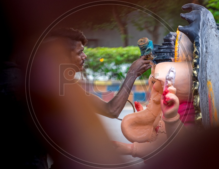 A person spraying the paint on the ganesha idols