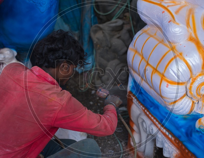 A person spraying the paint to the ganesha idol