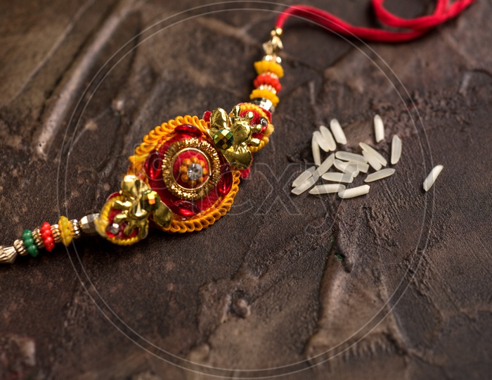 Elegant Rakhi With Rice Grains On an Textures Background For Raksha Bandhan Festival