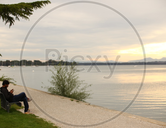 A Man using Mobile smartphone While Sitting On a Lake bank