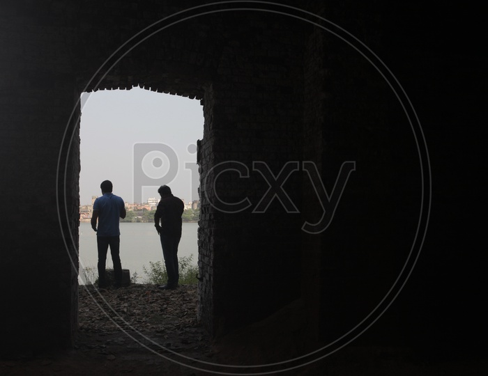 A Couple Of Men Standing  On the Bank  Of a Lake