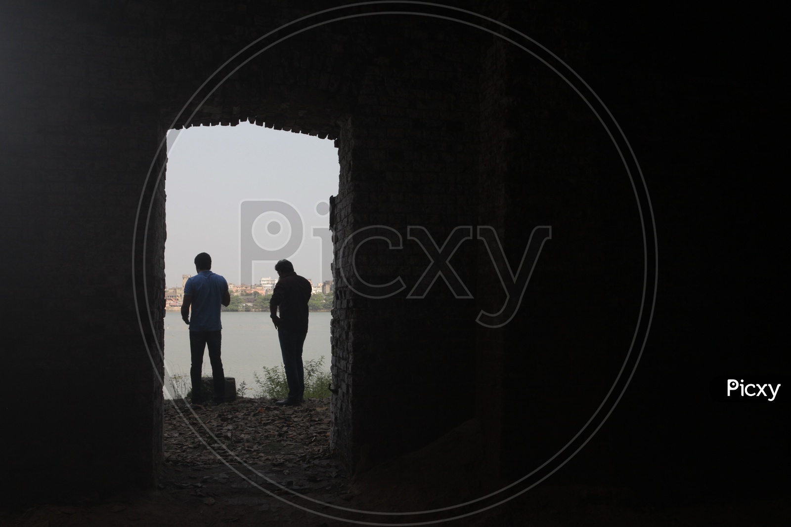A Couple Of Men Standing  On the Bank  Of a Lake