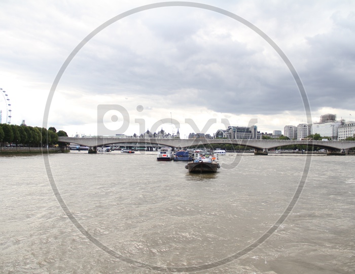 Unidentified Boats crossing a Bridge on Thames River with Clouds in Background