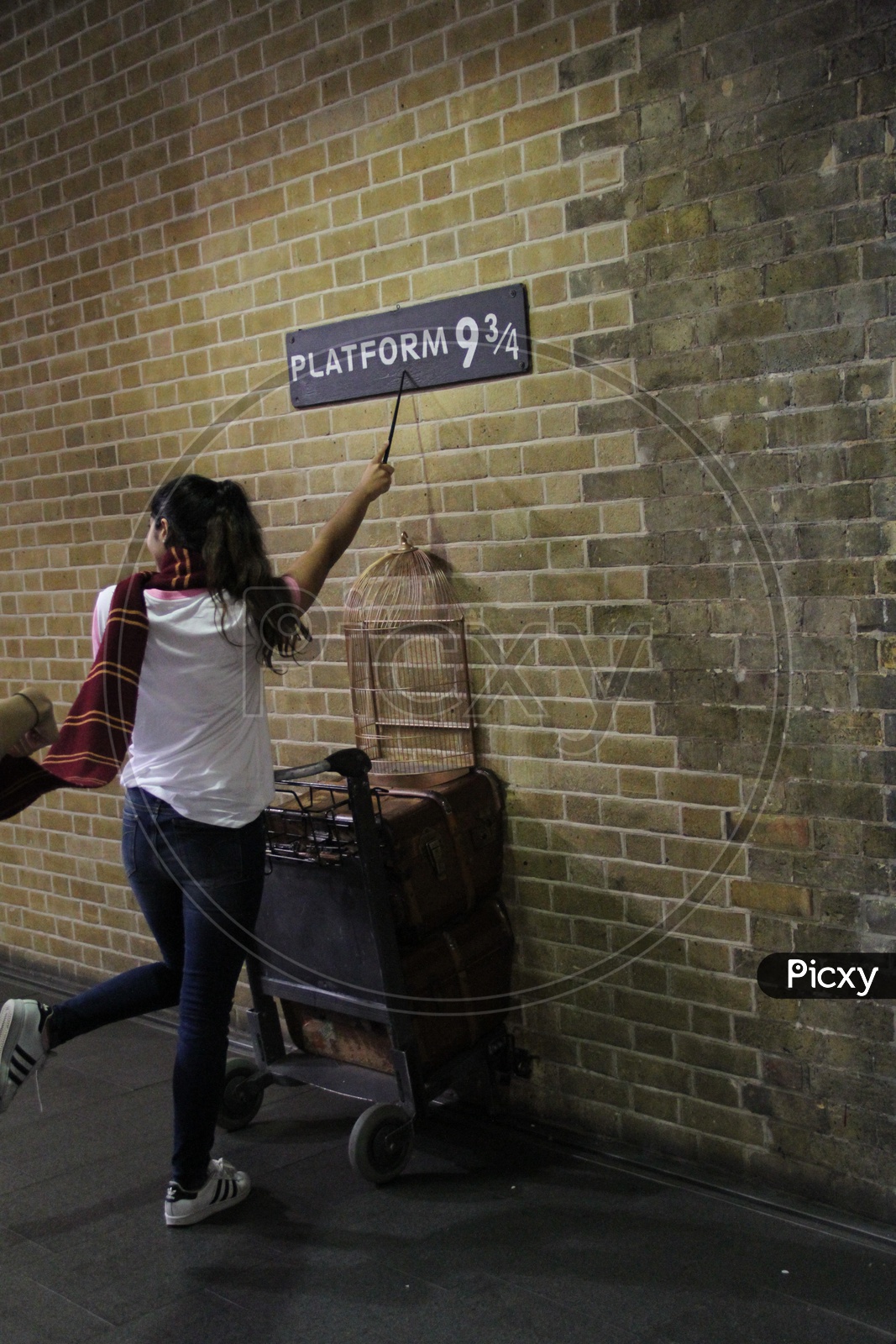 Young Woman with Magic wand  Pointing at Platform 9 3/4 Sign from Harry Potter movie in King's Cross Station