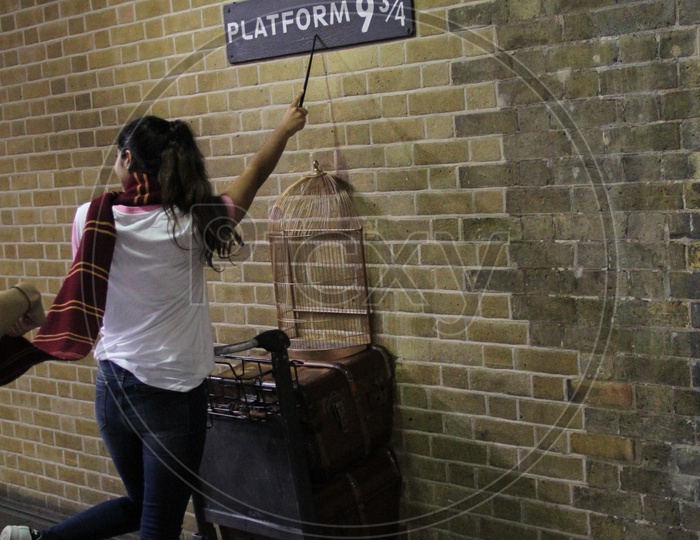 Young Woman with Magic wand  Pointing at Platform 9 3/4 Sign from Harry Potter movie in King's Cross Station