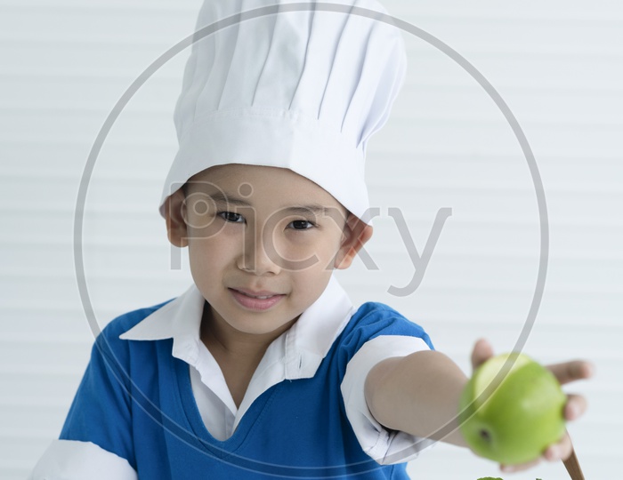 Boy as chef enjoying cooking with green apple in hand