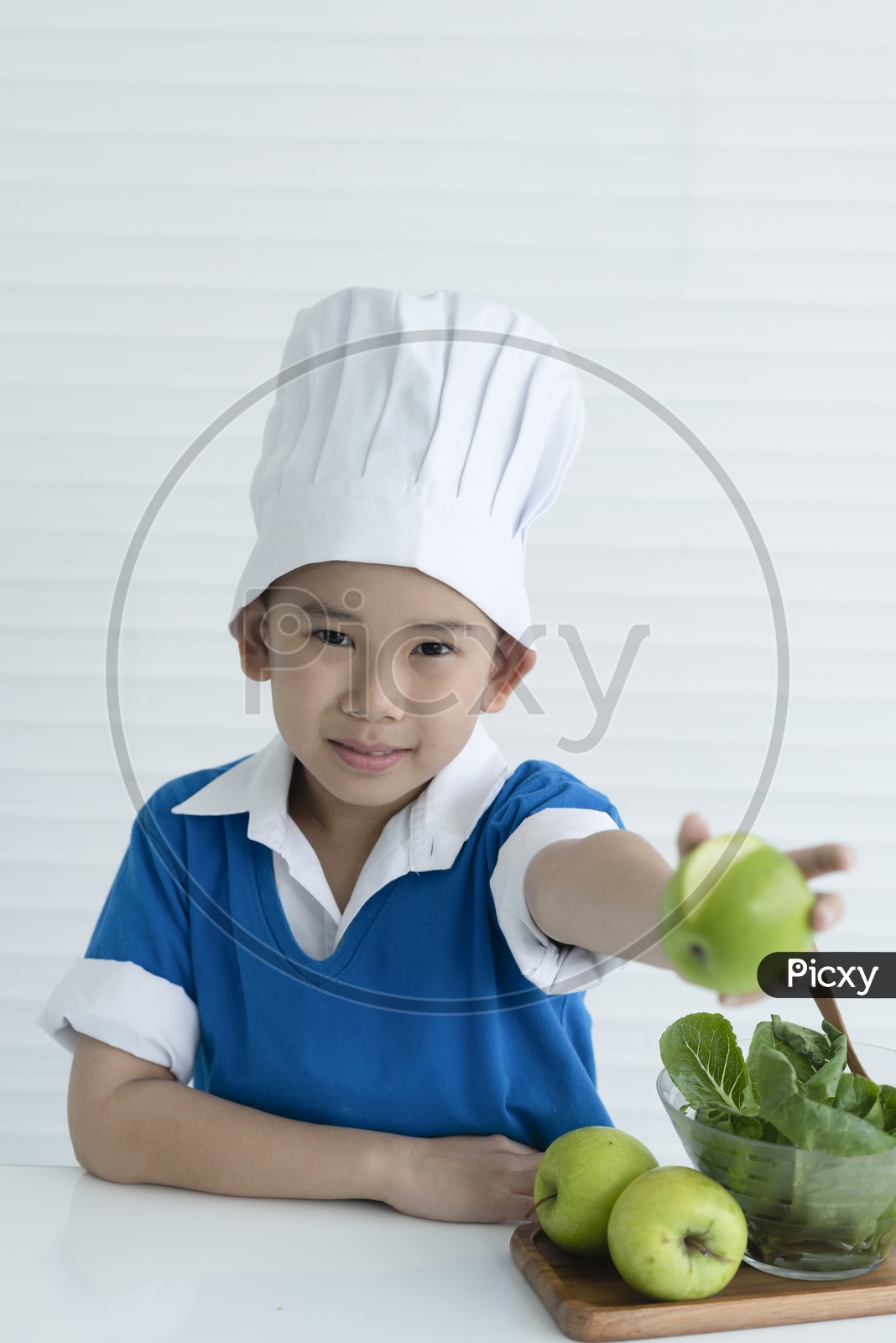 Boy as chef enjoying cooking with green apple in hand