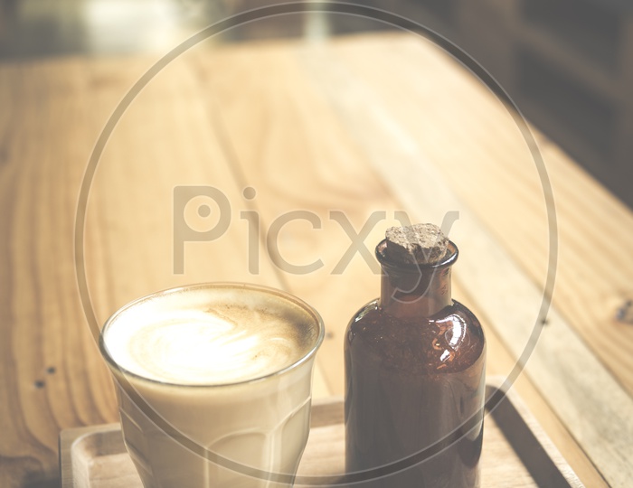 Coffee Latte Art On a Coffee With Sugar Syrup Bottle On Cafe Wooden table Background And with Vintage Filter