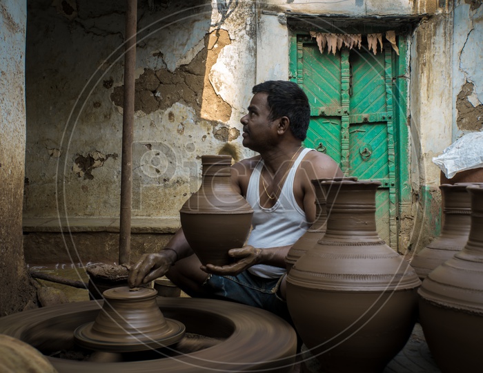 Pottery worker preparing pots on wheel with a set of freshly prepared pots beside him.