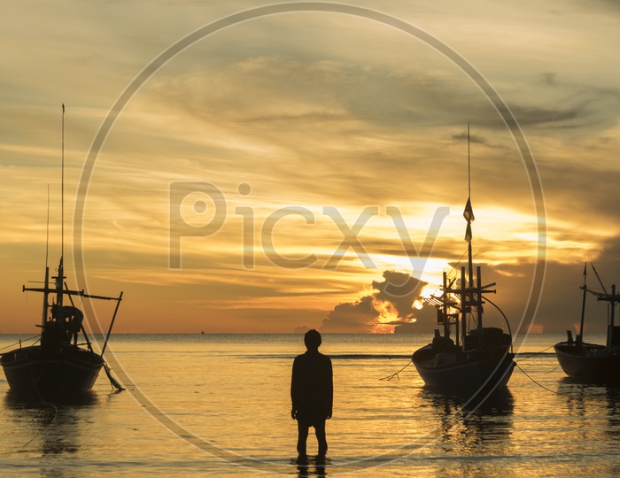 Fishing Boats In a Beach With  Fisherman Carrying Their Catch Over a Golden Sunset Sky In Background