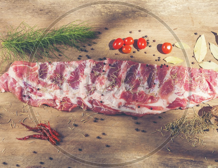 Top view of raw ribs with a rosemary and vegetables on wooden chopping  board