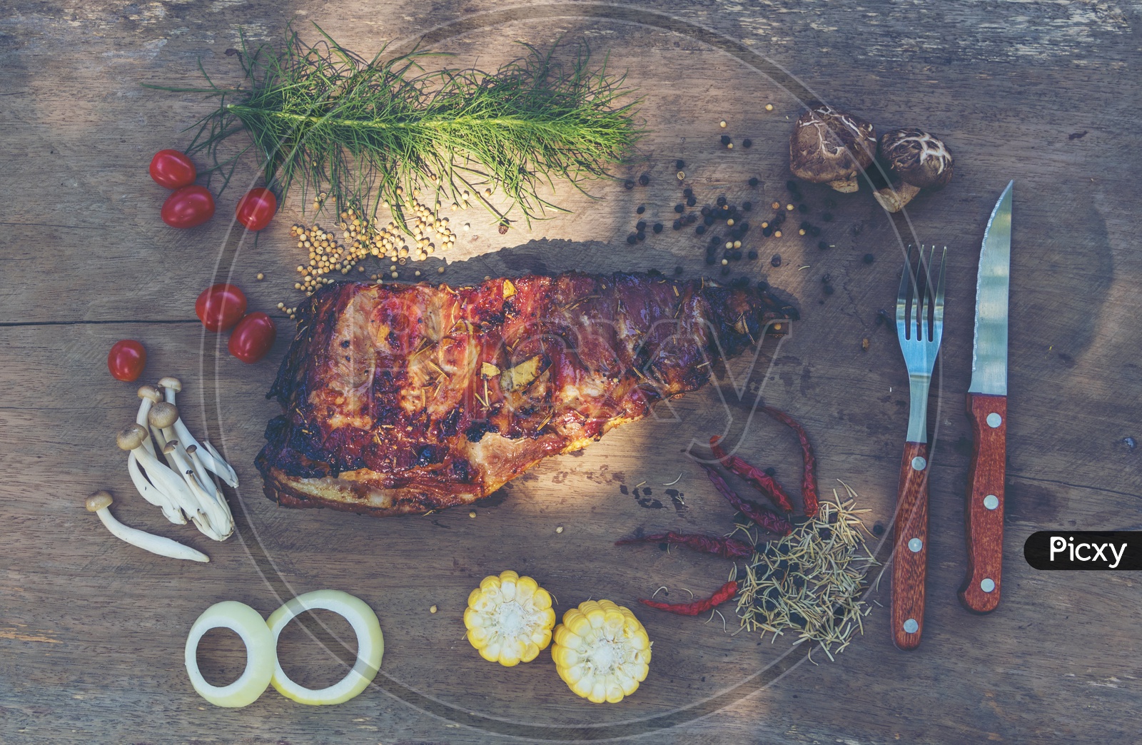Top view of spicy hot grilled spare ribs from a summer BBQ served with a hot chili pepper and fresh tomatoes on an old vintage wooden cutting board