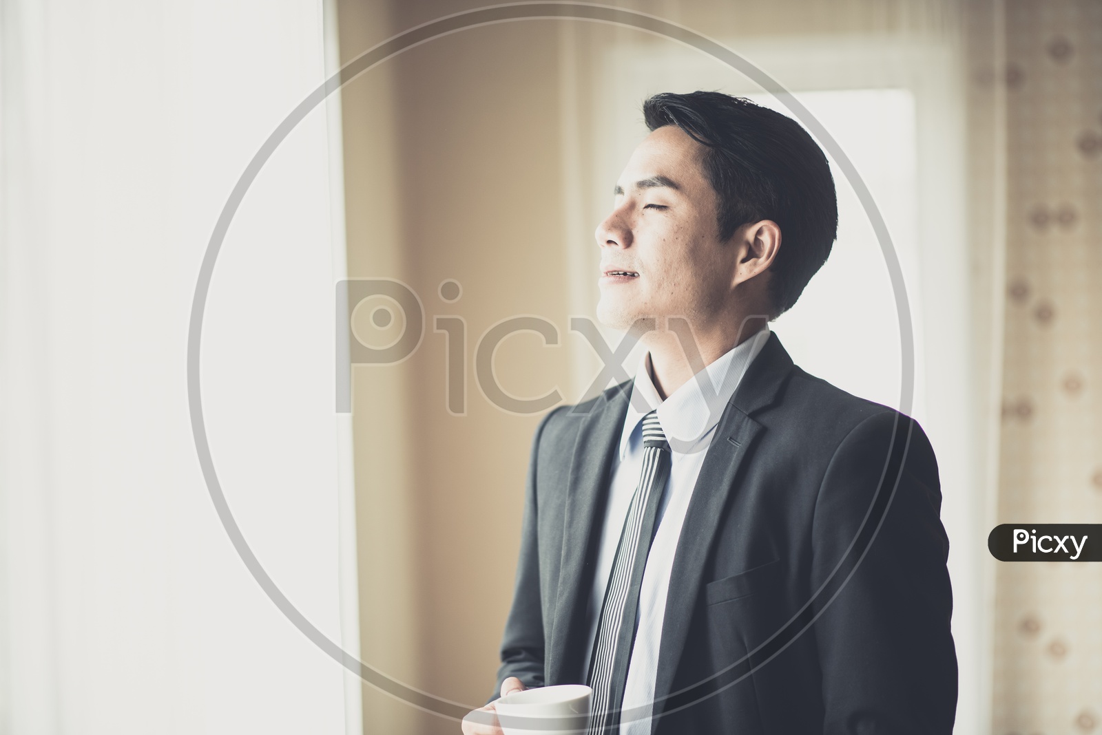 Young Businessman Enjoying Coffee and Sunshine From a Office room Window