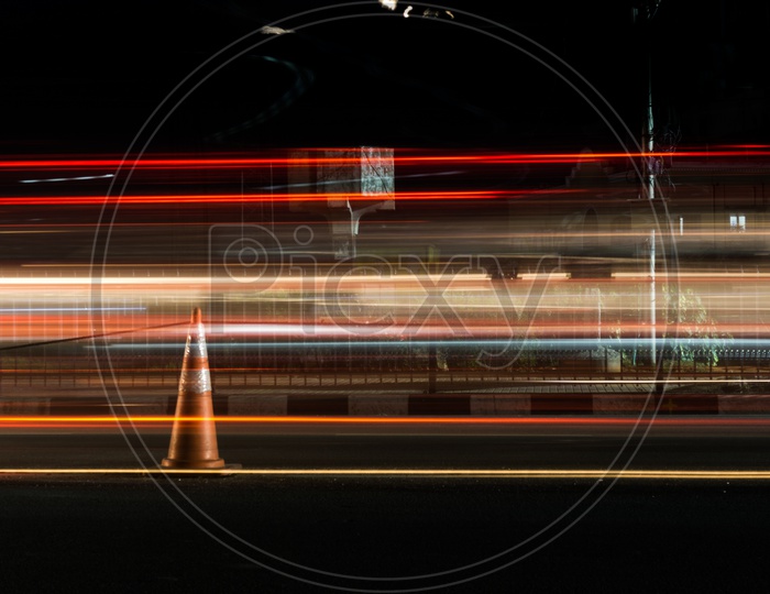Traffic safety cone, with long exposure light painting of vehicle running on either side of it.