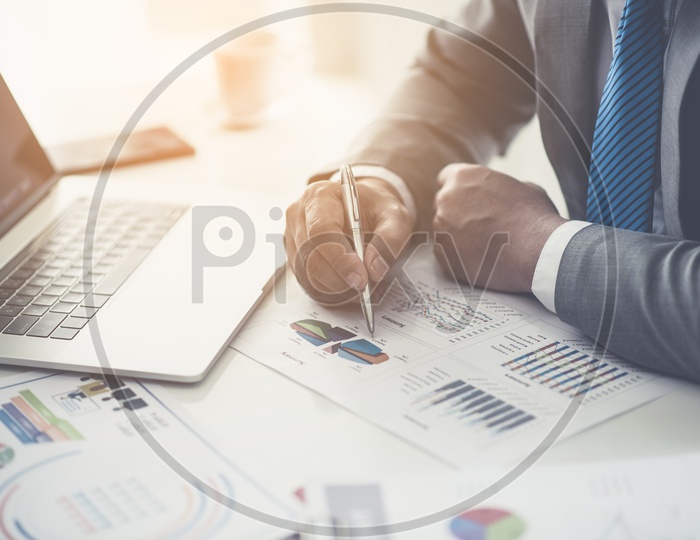 Businessman Verifying Statistics and Charts  Of Business Growth Over a office desk Backdrop