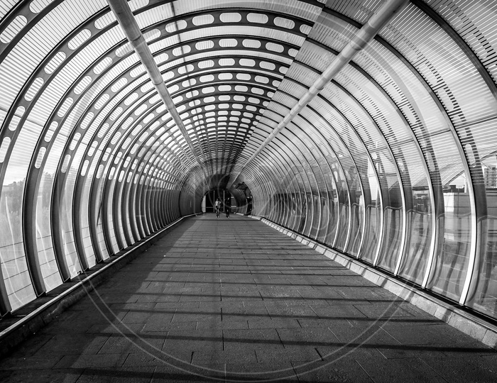 Vortex like Pedestrian bridge built with glass and steel and two women friends walking down during evening sunset of summer in canary wharf of London