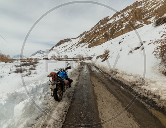 A Biker Parked his bike alongside Road covered in Snow at Spiti Valley in Winters