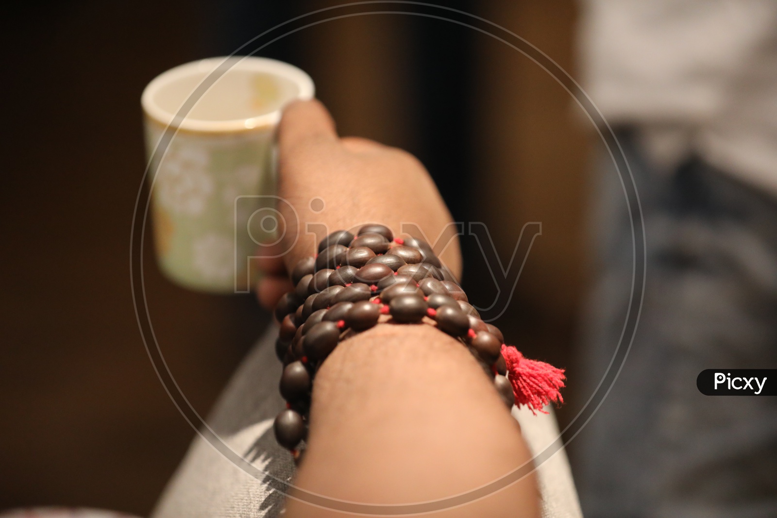 A man holding a coffee mug wearing beaded bracelet