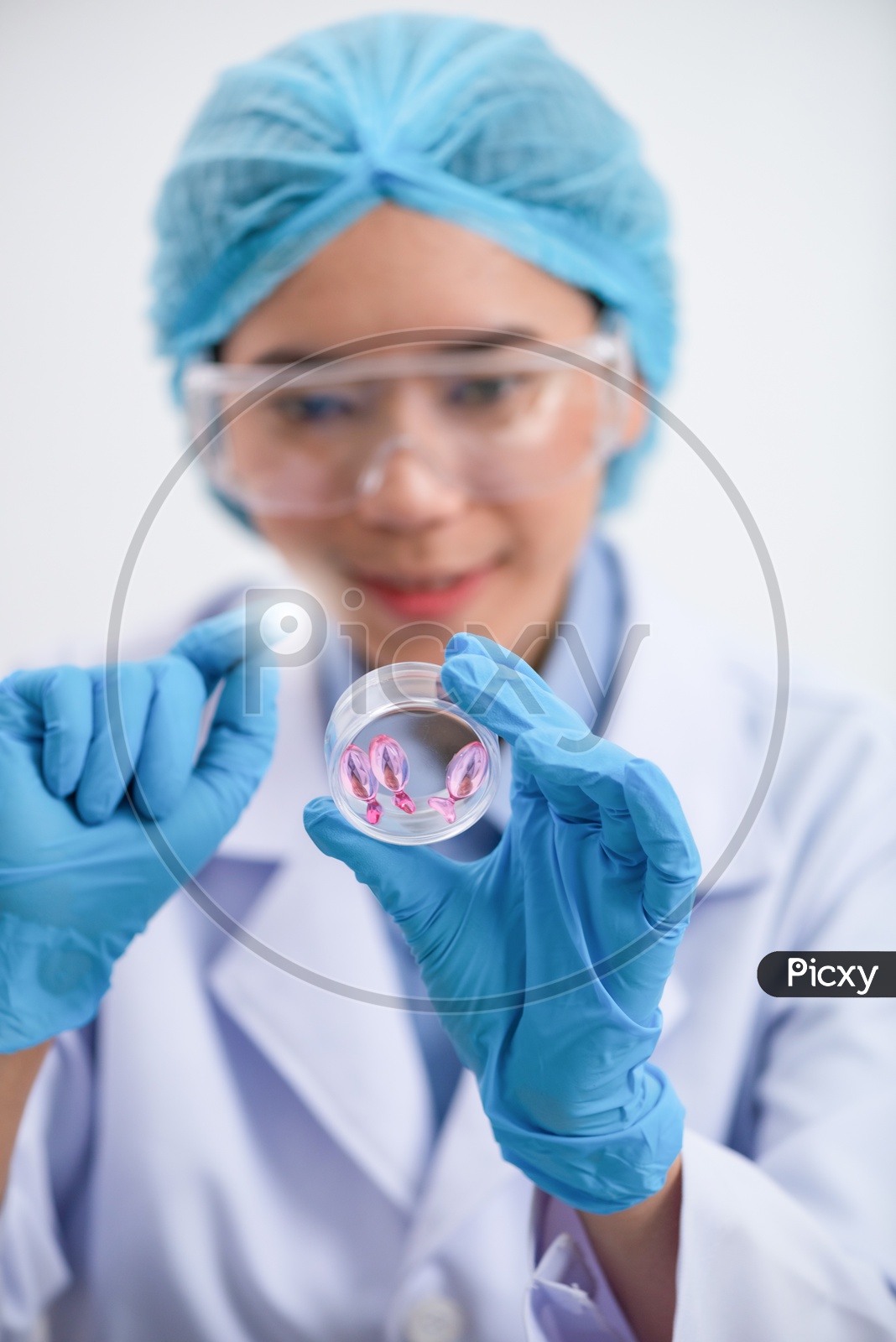 Young female scientist with protective eyeglasses and mask holding a Vitamin Capsule
