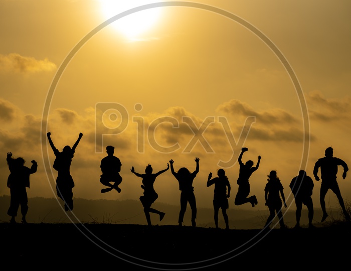 The silhouette of a group of people Jumping in joy Over Sunset Sky