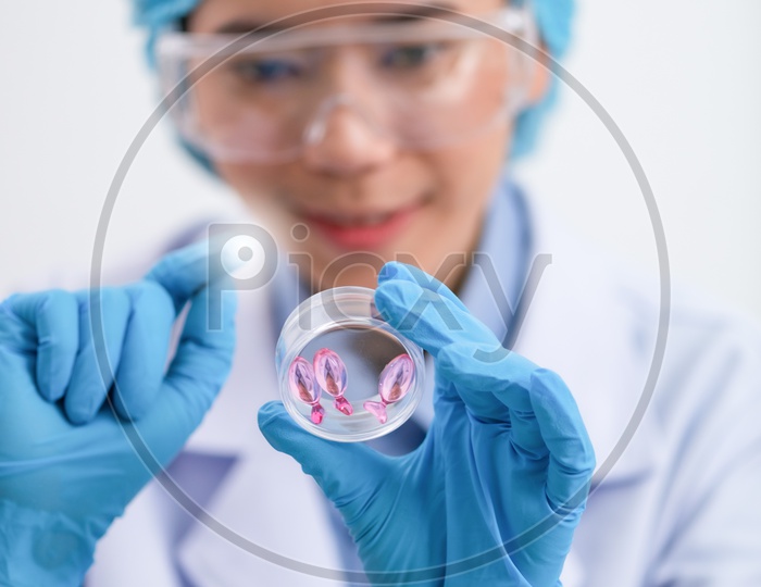Young female scientist with protective eyeglasses and mask holding a Vitamin Capsule