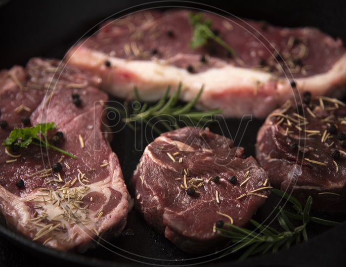 raw beef steaks With Spices Topped On a Cooking Pan Background