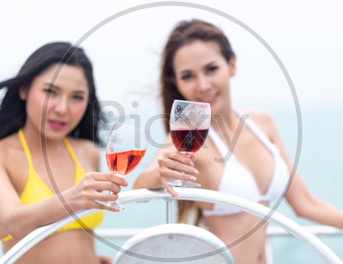 Asian Bikini Models holding wine in a glass on a yacht