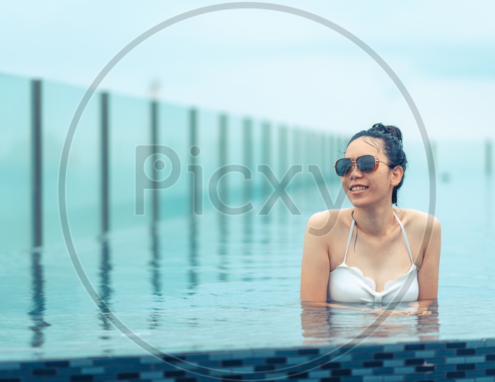 Asian girl wearing swimsuit and sunglasses in Swimming pool on roof top