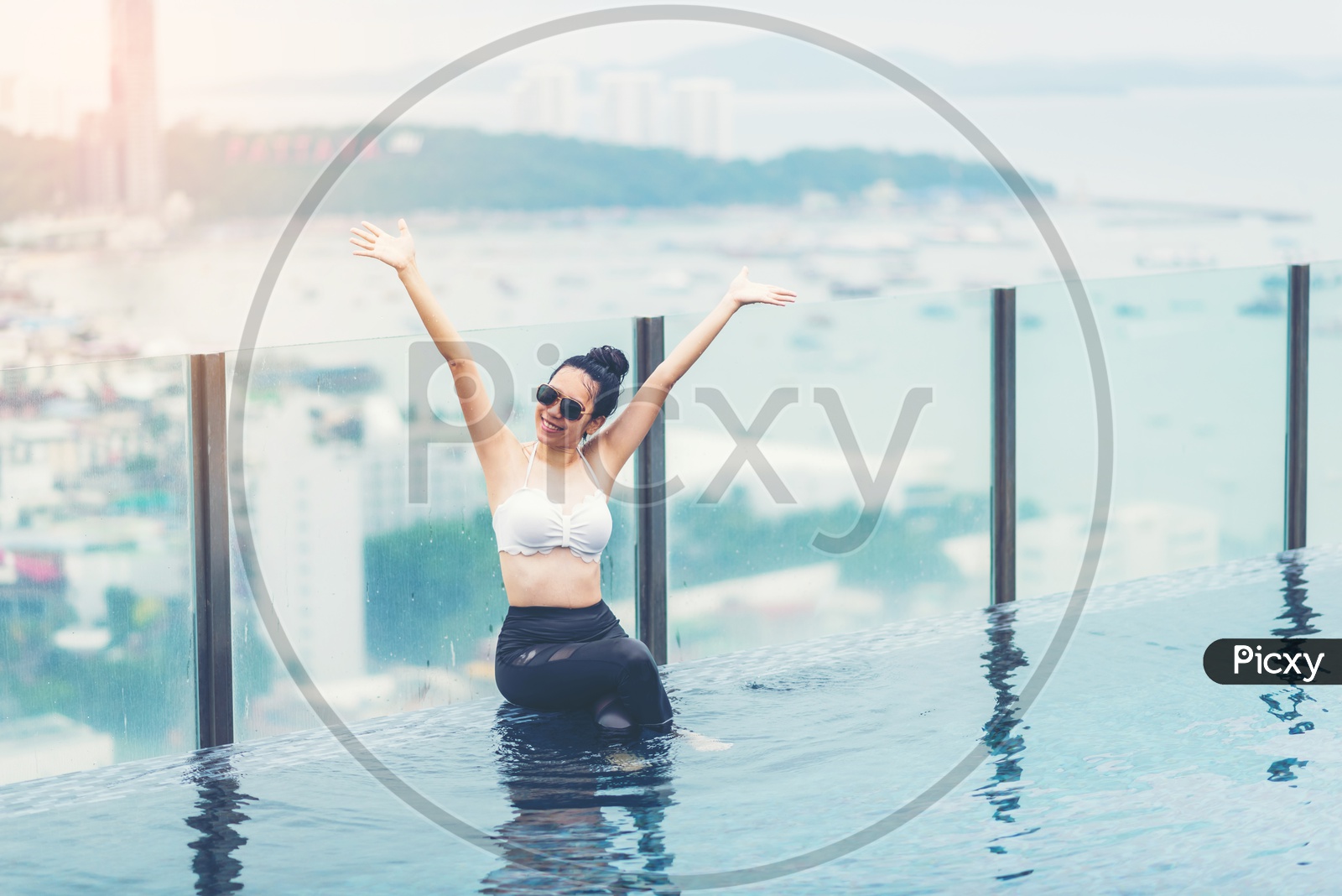An Asian girl cheering in Swimming pool on roof top with beautiful city and sea view