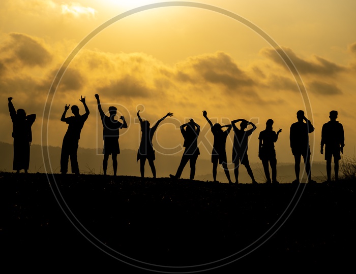 silhouette of  group of people is celebrating success on the hilltop Over Sunset Sky In Background