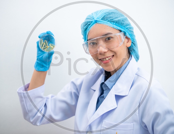 Young female scientist with protective eyeglasses and mask holding a transparent pill