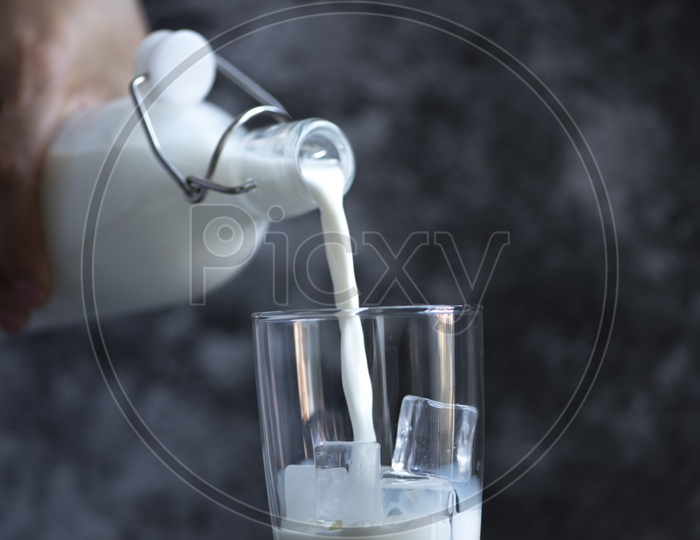 Pouring fresh milk into a glass with ice.